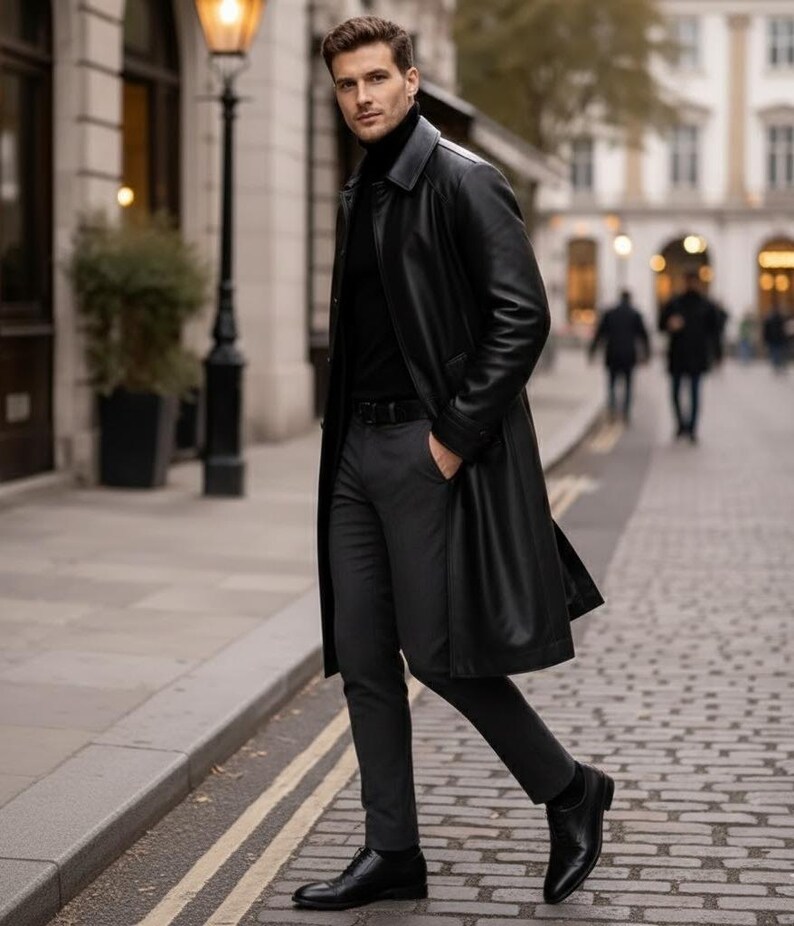 May include: A black leather trench coat with a matching black turtleneck and dark gray trousers. The coat is knee-length and has a classic design. The outfit is completed with black leather shoes. The person is walking on a cobblestone street.