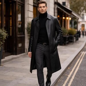 May include: A black leather trench coat with a classic design. The coat features a button-down front, a collar, and pockets. The person in the image is wearing a black turtleneck, gray pants, and black shoes. The background shows a city street.