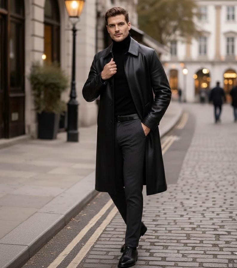 May include: A black leather trench coat, black turtleneck, and dark gray trousers. The coat is buttoned at the top and worn over a black turtleneck. The trousers are paired with black dress shoes. The outfit is completed with a black belt.