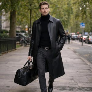 May include: A black leather trench coat with a matching black leather duffel bag. The coat is buttoned and worn over a black turtleneck and gray pants. The person is walking on a city sidewalk.