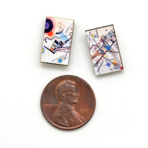 Small rectangle stud earrings featuring Kandinsky geometric art in a rainbow of circles, lines and squiggles. The earrings are next to a copper USA penny showing the earrings are smaller than the penny.