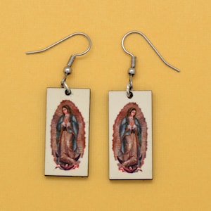These rectangle earrings feature an image of the iconic Virgin of Guadalupe. The image is reversed on the two earrings so they can face each other or look away from each other. The background is beige.