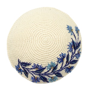 This is a round crochet yarmulke that the base is a off white  natural color.  Around about 45% of the edge, there are embroidered blue leaves with dark and light blue flowers. The leaves and flowers have tiny accent beads of blue and bronze.