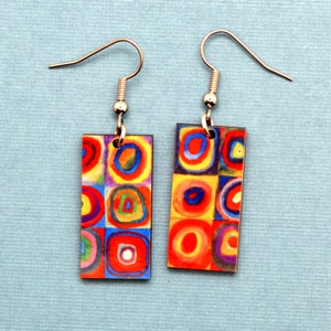 Each earring has squares, that are filled with circles. They are created with imperfect circles in a rainbow of colors including orange, red, blue, yellow, purple and green. The earrings are shown on a light blue background.