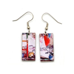 May include: Rectangular dangle earrings with a colorful, artistic design. Each earring features a unique print with cityscapes, a cat, and abstract figures. The earrings have silver-tone hooks for pierced ears.