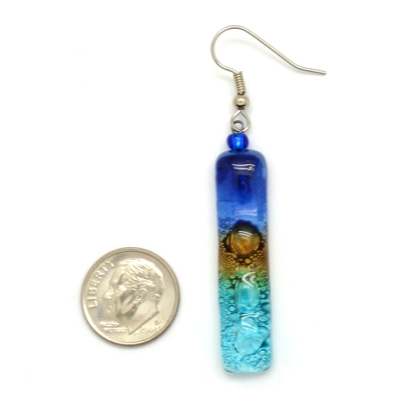 Skinny rectangle glass blue earrings. The earrings are next to a USA dime showing the earrings are more narrow than a dime, and much taller than the dime.