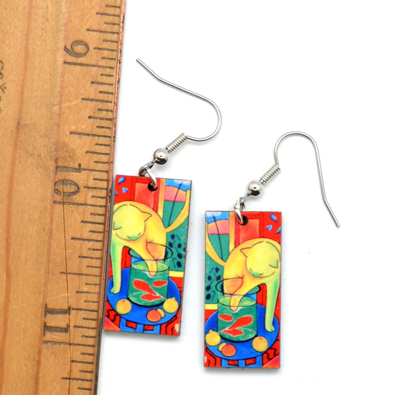 Matisse Cat earrings shown next to a ruler. It shows the earrings are approximately 1-1/8 inch long and also shows the fish hook ear wires.