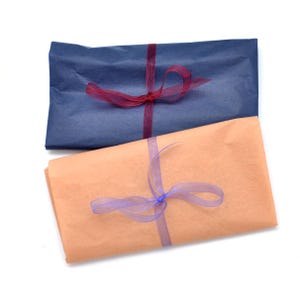 Pode incluir: Dois presentes embrulhados, um em papel azul marinho e outro em papel cor de p&ecirc;ssego. Cada um &eacute; amarrado com uma fita transparente, uma bord&ocirc; e outra lavanda. Os presentes est&atilde;o dispostos sobre um fundo branco.