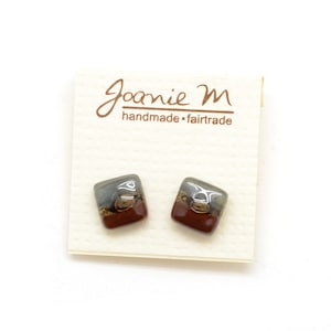 May include: A pair of square stud earrings featuring a glossy finish with a color gradient transitioning from dark gray at the top to deep reddish-brown at the bottom. The earrings are displayed on a cream-colored card labeled Joanie M handmade fairtrade.