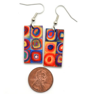 The rectangle Kandinsky painting earrings are shown with a USA penny. This the penny is wider than the earrings and not as tall as the earrings.