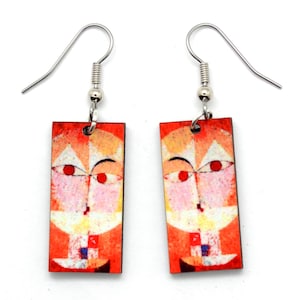 May include: A pair of rectangular earrings with a colorful abstract face design. The earrings feature a red, orange, and white color palette with silver-tone ear wires. The artwork on the earrings has a modern art style.