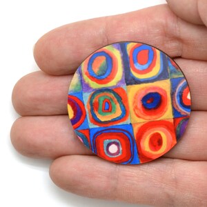 May include: A round wooden pin with a colorful abstract design featuring circles and squares in shades of red, yellow, blue, green, and purple.