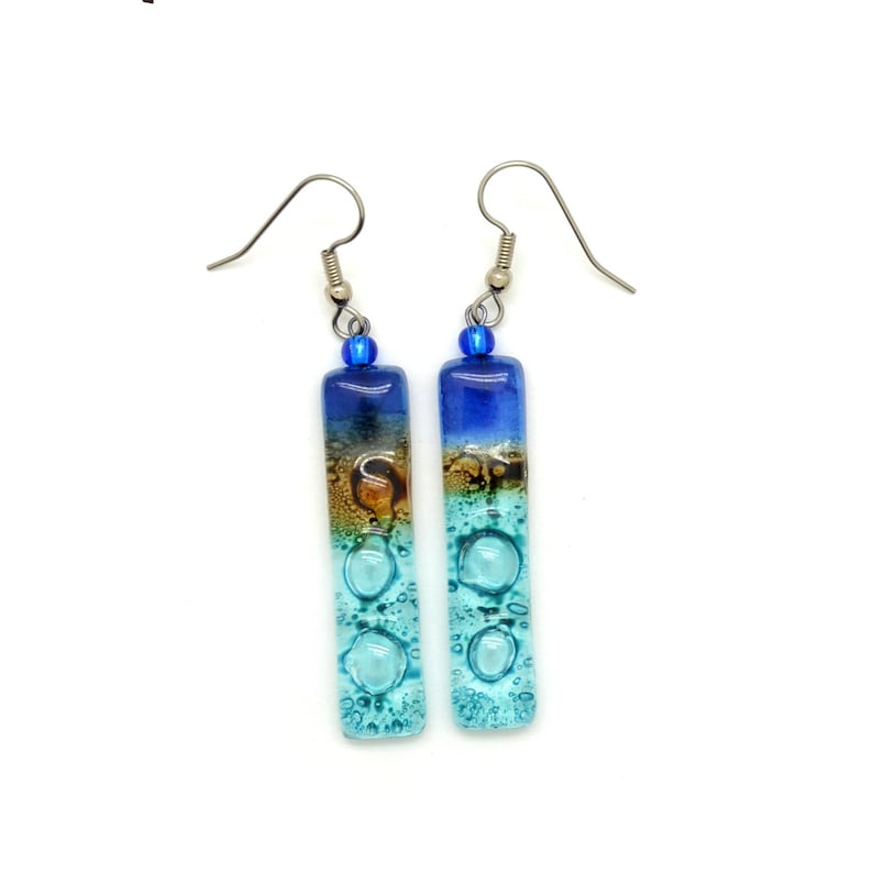 Skinny rectangle glass blue earrings. The very top has a cobalt blue glass bead. The fused glass is in three bands of color. At the top is dark cobalt blue. Second, bronze. Third and widest is an aqua turquoise color. The glass has bubbles.