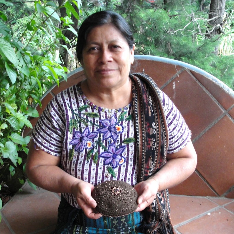 An artisan shows off a kippa she made. She is smiling and wearing a traditional Guatemalan blouse.