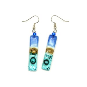 Skinny rectangle glass blue earrings. The very top has a cobalt blue glass bead. The fused glass is in three bands of color. At the top is dark cobalt blue. Second, bronze. Third and widest is an aqua turquoise color. The glass has bubbles.