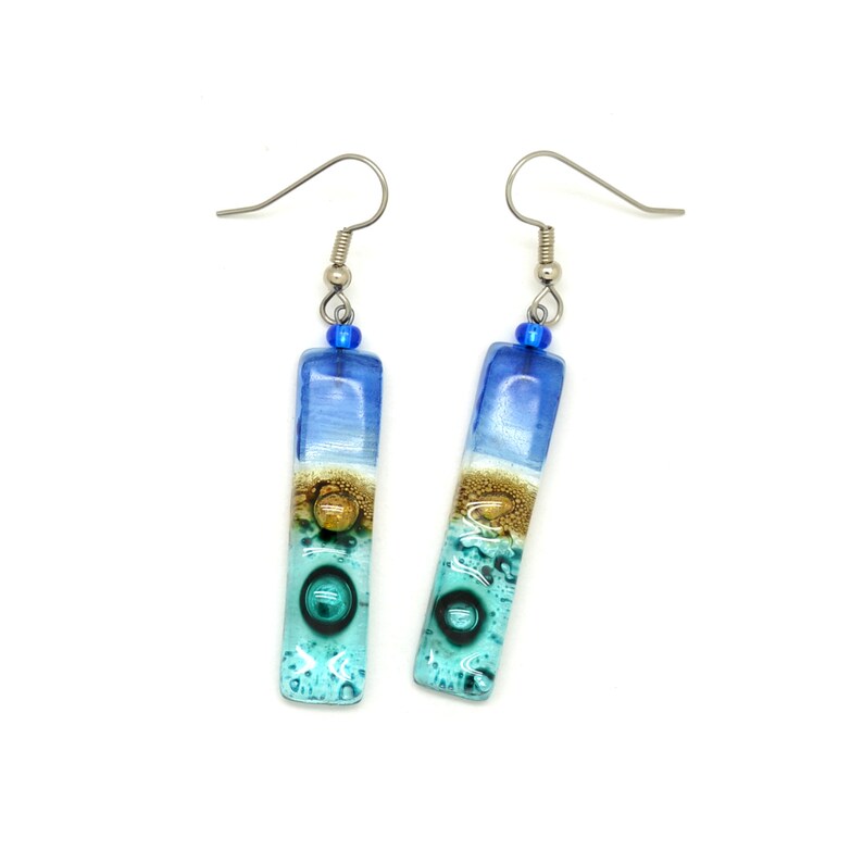Skinny rectangle glass blue earrings. The very top has a cobalt blue glass bead. The fused glass is in three bands of color. At the top is dark cobalt blue. Second, bronze. Third and widest is an aqua turquoise color. The glass has bubbles.