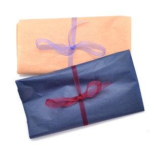 May include: Two wrapped parcels, one in tan paper tied with a purple ribbon, and another in navy blue paper with a burgundy ribbon. The parcels are on a white background.