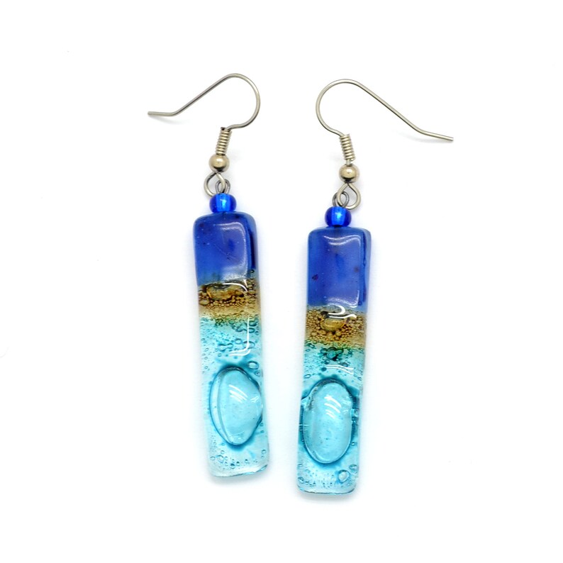 Skinny rectangle glass blue earrings. The very top has a cobalt blue glass bead. The fused glass is in three bands of color. At the top is dark cobalt blue. Second, bronze. Third and widest is an aqua turquoise color. The glass has bubbles.