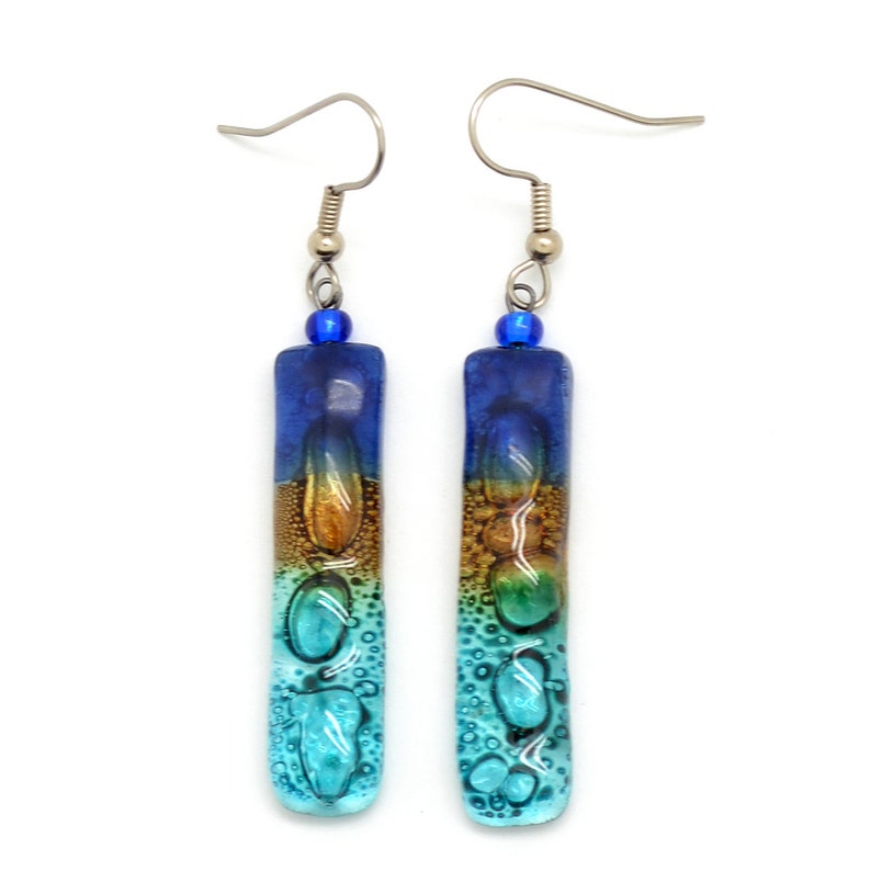 Skinny rectangle glass blue earrings. The very top has a cobalt blue glass bead. The fused glass is in three bands of color. At the top is dark cobalt blue. Second, bronze. Third and widest is an aqua turquoise color. The glass has bubbles.
