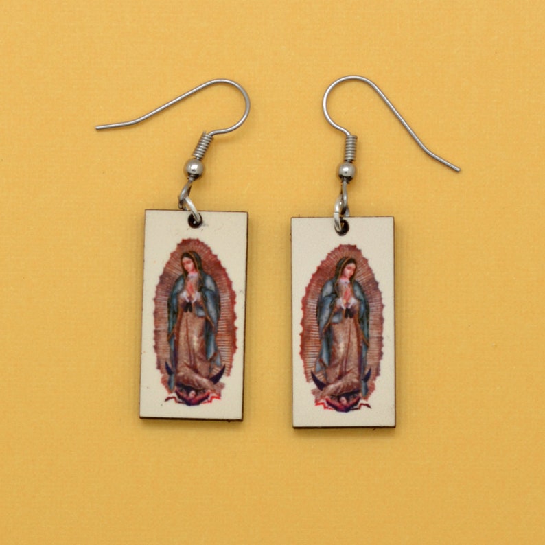 These rectangle earrings feature an image of the iconic Virgin of Guadalupe. The image is reversed on the two earrings so they can face each other or look away from each other. The background is beige.