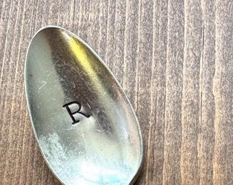 May include: A silver spoon with an ornate design on the handle. The spoon has the letter "R" engraved on the bowl.