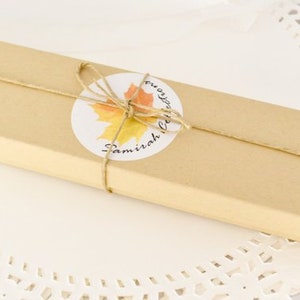 May include: A brown cardboard box with a twine bow and a round sticker with a yellow and orange leaf design. The sticker says "Samirah Creations".