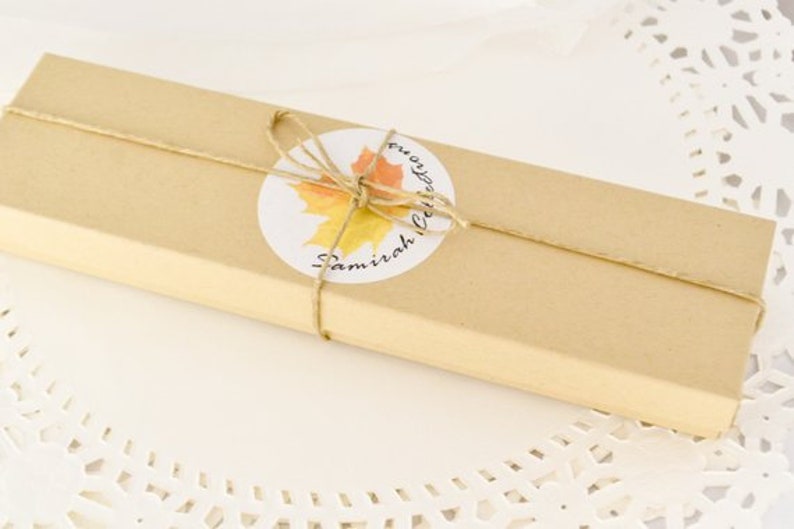 May include: A brown cardboard box with a twine bow and a round sticker with a yellow and orange leaf design. The sticker says "Samirah Creations".