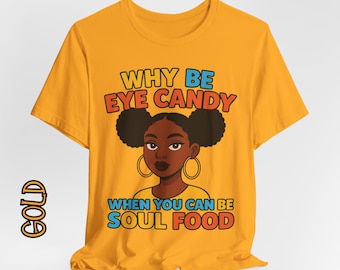 May include: Mustard yellow t-shirt with the text "WHY BE EYE CANDY WHEN YOU CAN BE SOUL FOOD" above a cartoon illustration of a Black woman with two buns and gold hoop earrings.