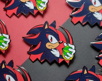 May include: A set of five enamel pins featuring Shadow the Hedgehog from the Sonic the Hedgehog video game series. Each pin depicts Shadow holding a green Chaos Emerald. The pins are red, black, and green.