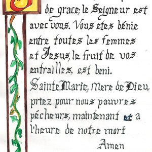 May include: A handwritten prayer in black ink on white paper with a decorative initial letter in red and yellow. The text reads: "J e vous salue, Marie pleine de grace; le Seigneur est avec vous. Vous etes bénie entre foutes les femmes et Jesus, le fruit de vos entrailles, est beni. Sainte Marie, Mere de Dieu, priez pour nous pauvres pécheurs, maintenant et a l'heure de notre mort Amen."