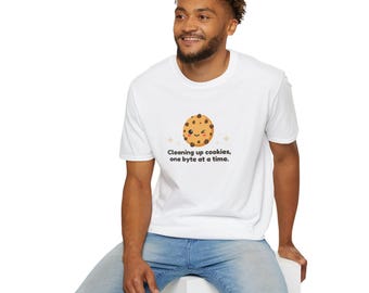 Può includere: T-shirt bianca con un biscotto dei cartoni animati con un volto sorridente e gocce di cioccolato. Il testo "Cleaning up cookies, one byte at a time" è stampato sotto. La maglietta è indossata da una persona.