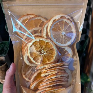May include: A clear plastic bag filled with dried orange slices. The orange slices are stacked on top of each other and are a light orange color.