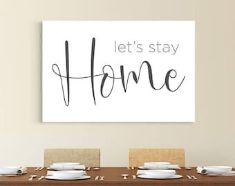 May include: A white canvas print with the text "Let's stay home" in a gray cursive font. The print is hanging on a wall above a wooden dining table with four chairs and a bench.