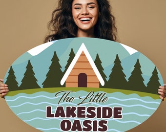 May include: A woman holds a blue and green oval sign with a cartoon cabin, trees, and the text "The Little Lakeside Oasis".