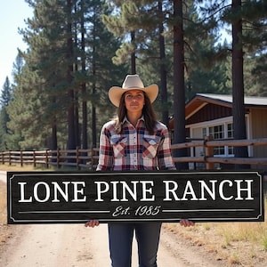 May include: A woman wearing a cowboy hat and a checked shirt holds a black sign with white text that reads "Lone Pine Ranch Est. 1985".