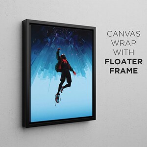 Op de afbeelding: Een canvas print met een zwarte zwevende lijst met daarop een persoon in een rood en zwart pak die in de lucht springt tegen een blauwe en witte stadsachtergrond.