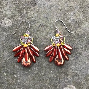 May include: A pair of dangle earrings with a cluster of red, green, and clear beads. The earrings have a silver hook.