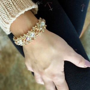 Peut inclure: Un bracelet en perles dorées avec des cristaux transparents et ambrés. Le bracelet est porté au poignet.
