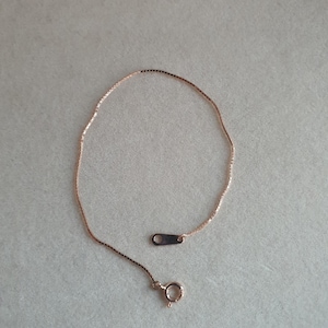 Op de afbeelding: Een delicate roségouden kettingarmband met een box chain design. De armband heeft een kleine sluiting en een rechthoekige connector. De ketting wordt gepresenteerd op een neutrale achtergrond.