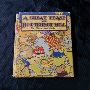 May include: A vintage book cover with a colorful illustration of animals having a feast on Butternut Hill. The title is "A Great Feast on Butternut Hill" by Harrison Cady. The book is published by Whitman Publishing Company in Racine, Wisconsin.