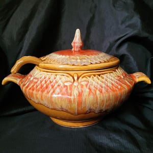May include: A vintage ceramic soup tureen with a lid. The tureen is a warm brown color with orange and yellow accents. It has two handles and a decorative finial on the lid. The tureen is likely from the mid-century era.
