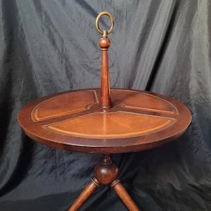 May include: A round, wooden table with a leather top and three legs. The table has a brass ring on top of a wooden post in the center.