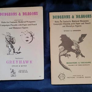 May include: Two vintage "Dungeons & Dragons" rulebooks. The book on the left is titled "Greyhawk" and features a warrior illustration. The book on the right is titled "Monsters & Treasure" with a dragon illustration. Both are printed on off-white paper.
