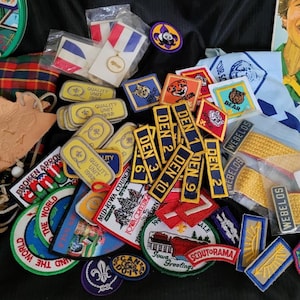 May include: A collection of colorful embroidered patches featuring various scouting themes, including "Den 1", "Den 2", "Den 3", "Den 9", "Den 10", "Webelos", "Scoutorama", "Quality Unit 1992", "Mid-Iowa Council", "Iowa Corn", "Broken Arrow", "The World", "Sail Boat Build and Grow with Lowe's", and "Bear".