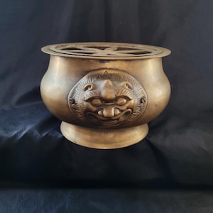 May include: A brass incense burner with a decorative lion's head design. The burner has a round base and a circular top with a grill.