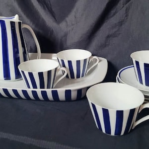 May include: A white serving tray with blue stripes and a matching pitcher and four cups and saucers. The cups and saucers are also decorated with blue stripes.