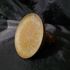 May include: A brass shower head with a round, flat face and numerous small holes. The shower head has a worn, aged appearance.