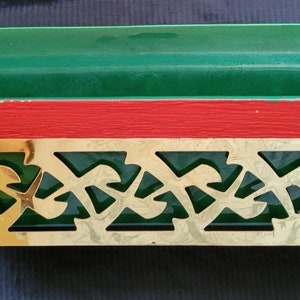 May include: A green and red planter with a gold metal decorative trim. The planter has a rectangular shape and is made of metal.