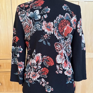 May include: Black jacket with a floral design in red, white, and blue. The jacket has a shawl collar and three-quarter sleeves. The floral pattern covers the back and sleeves of the jacket.