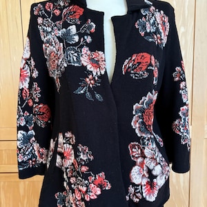 May include: Black open-front jacket with a floral pattern in red, white, and gray. The jacket has three-quarter sleeves and a collar. The floral design is concentrated on the shoulders, sleeves, and lower front panels.